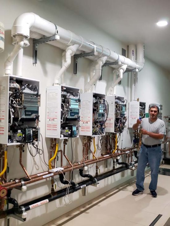 Training Workshop for Plumbing Professionals A plumbing instructor standing in a workshop with multiple tankless water heaters mounted for educational purposes.