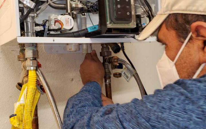 Technician adjusting valves on a modern water heater, showing intricate pipework and digital control units.