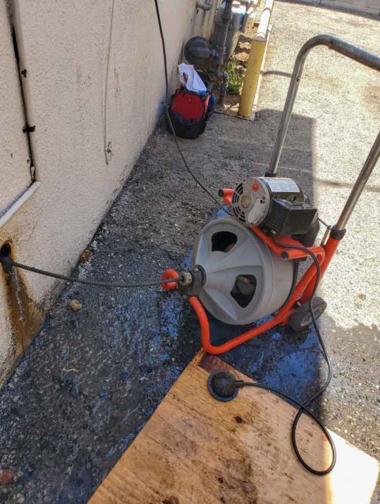 Portable Electric Drain Cleaning Machine Portable electric drain cleaning machine in operation outside, showing cables and water supply connected, ready for heavy-duty use.