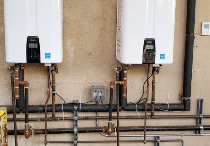Two high-capacity tankless water heaters installed on a wall, efficiently set up with multiple copper pipes and digital temperature controls.