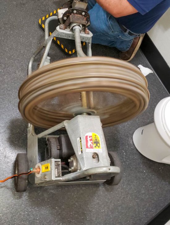 Professional Drain Cleaning Setup Industrial drain cleaning machine in operation with a rotating drum, used by a professional plumber during a service call.