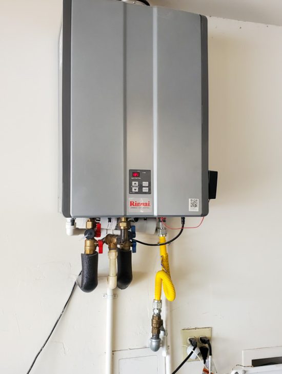 Efficient Residential Water Heating Rinnai tankless water heater installed on a white wall in a garage, with gas and water connections neatly organized.