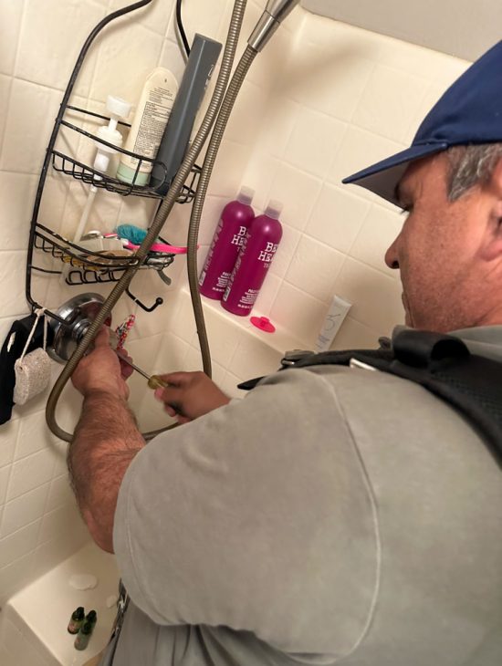 Professional Plumbing Maintenance Plumber adjusting a shower fixture in a residential bathroom, surrounded by various bath products.