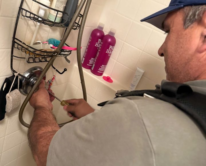 Plumber adjusting a shower fixture in a residential bathroom, surrounded by various bath products.