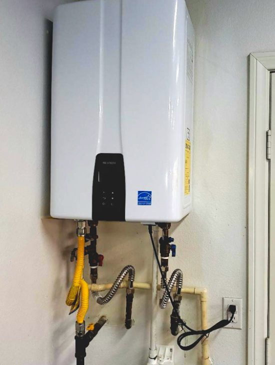 Sleek and Modern Water Heater Setup Sleek white tankless water heater installed against a textured wall with multiple connected pipes and cables.