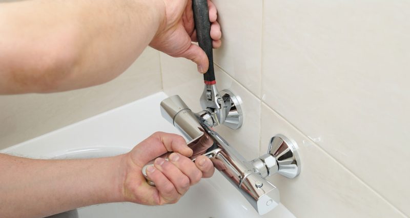 Plumber's hands installing a sleek new bathtub faucet, emphasizing detail and craftsmanship in modern plumbing.
